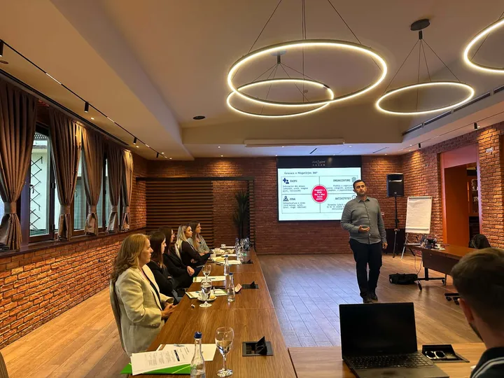 The trainer presents a session on risk assessment to journalists seated along a conference table at Hotel Dukagjini in Peja.